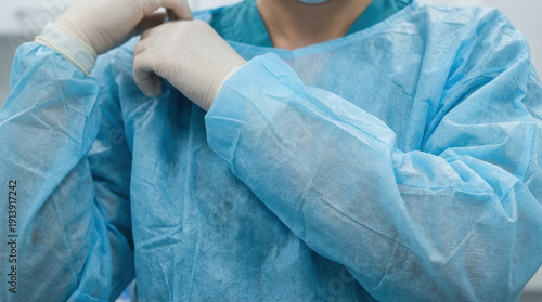 Blue disposable protective gown surgeon wearing gloves and preparing for procedure with focused calm expression