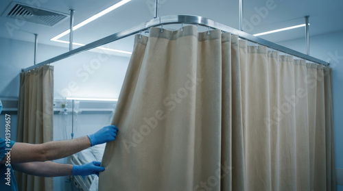 Hospital privacy curtain being drawn by gloved medical professional, clinical lighting and bed visible