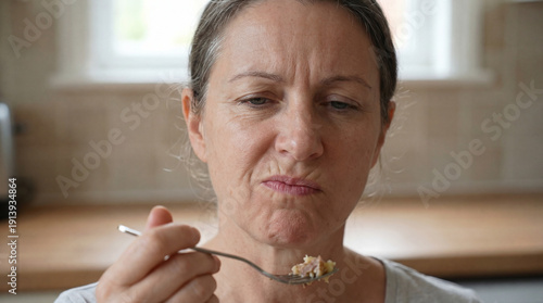 Grimacing woman discovers an unexpected and truly revolting flavor while sampling a meal in her bright kitchen