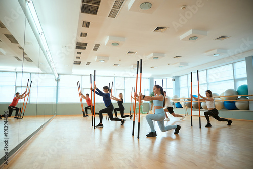 Men and women training with gymnastic sticks n athletic shoes in gym