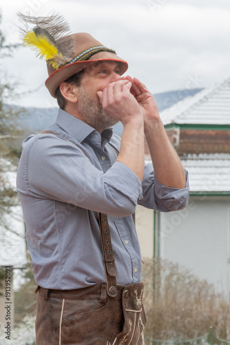 Adult man in Tyrolean hat performing yodel in Alpine village Austria