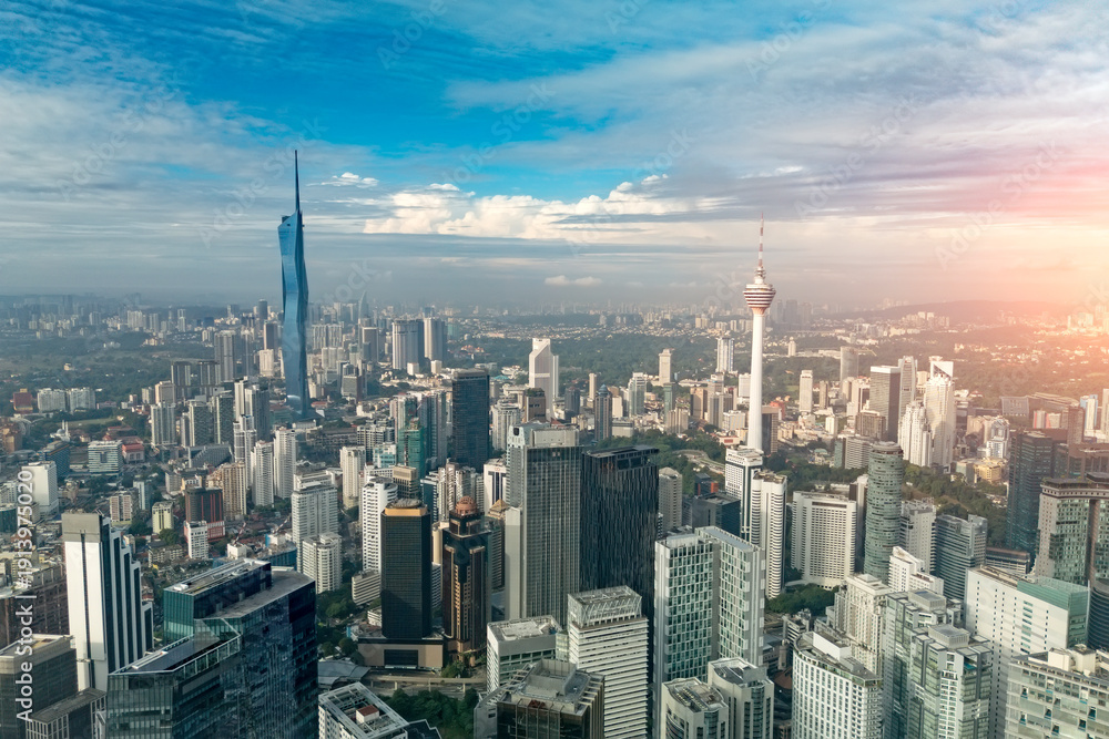 Fototapeta premium Expansive view of Kuala Lumpur, Malaysia, at sunrise. The city's many modern skyscrapers rise under a blue sky, featuring the iconic Kuala Lumpur Tower