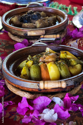 Traditional Moroccan table with two tajines filled with vegetables and meat, decorated with rose petals