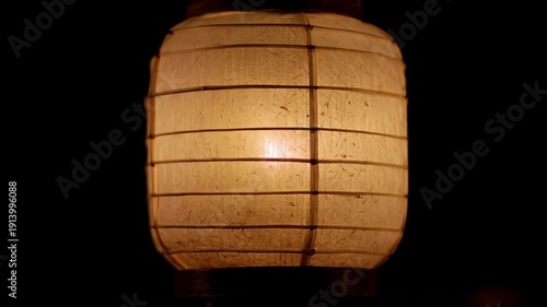 Glowing traditional japanese paper lantern, or chōchin, gently swaying in the dark night