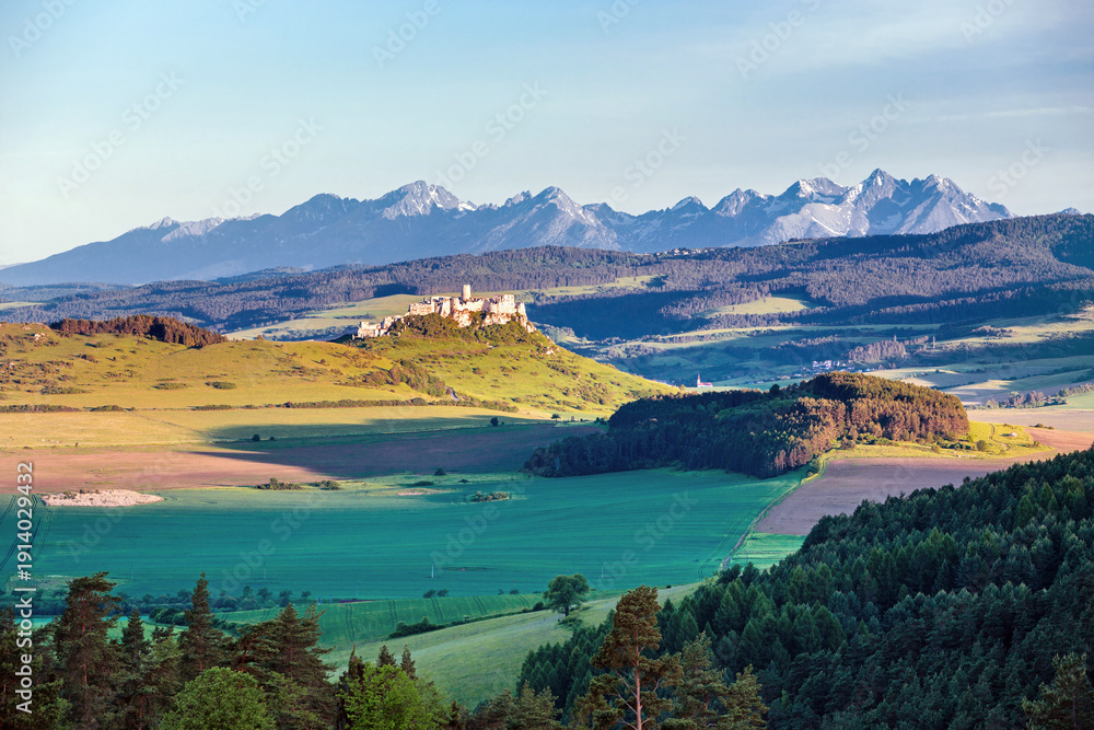 Naklejka premium Spiš Castle (Spišský hrad) in Slovakia, a historic stone fortress perched on a hilltop, with panoramic views of the surrounding mountains. Dramatic sky, vibrant colors, and natural light highlight the
