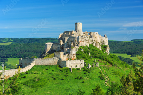 Spiš Castle (Spišský hrad) in Slovakia, a historic stone fortress perched on a hilltop, with panoramic views of the surrounding mountains. Dramatic sky, vibrant colors, and natural light highlight the
