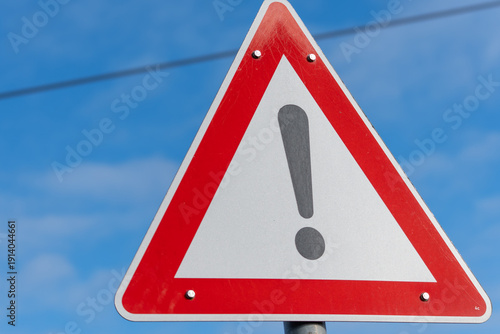 A red and white sign with an exclamation point on it. The sign is on a pole