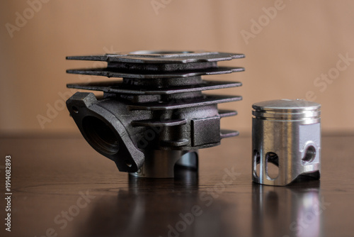 The photo shows a close-up of a metal cylinder with cooling fins and an engine piston. The parts are lying on a dark, flat surface.