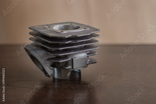The photograph shows a cylinder from an air-cooled internal combustion engine. The part is made of metal with characteristic fins for heat dissipation.