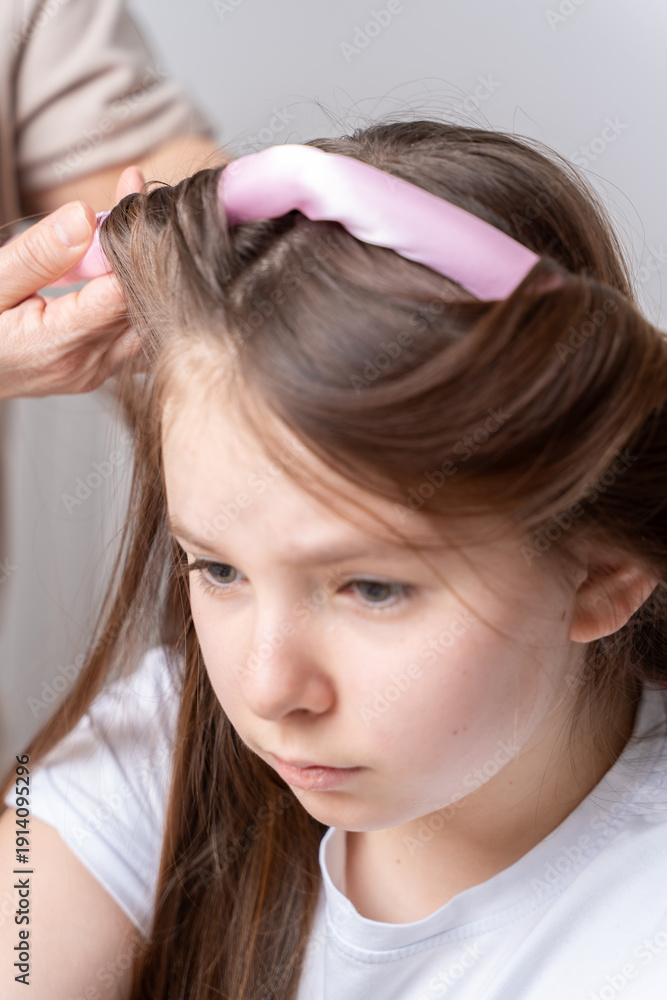 Fototapeta premium Mom's hands twist curlers for daughter in white T-shirt at home on a light background in front of the mirror
