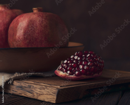 Ripe pomegranate with seeds on rustic wooden board in dark moody lighting
