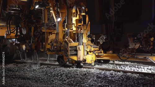 Close-up of a railway tamping machine working on track maintenance, compacting ballast and lifting the rails to correct alignment, restoring safe rail geometry at night