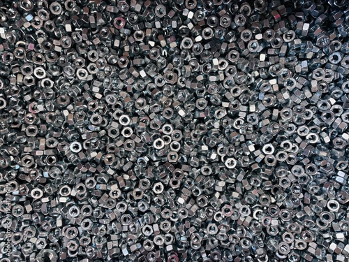 Top view background of a large group of silver metallic hex nuts. This industrial hardware texture features shiny steel fasteners, perfect for themes related to construction, mechanical engineering, a