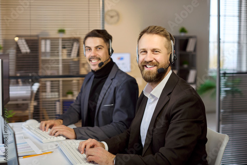 Call center agents with headset deliver service. Smiling operators in a modern office at computers resolve inquiries and sales with communication. Reliable support and customer care concept.