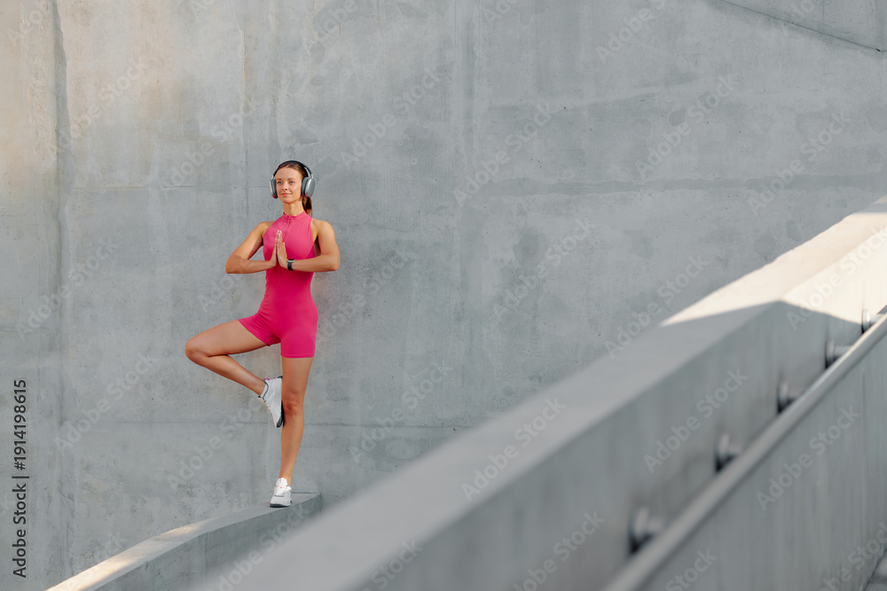 Fototapeta premium Young woman practicing yoga outdoors on a modern structure during daytime
