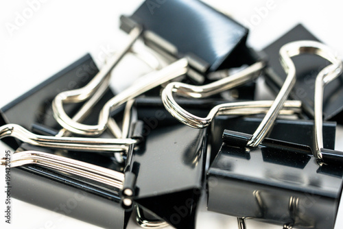 Black binder clips stacked on a white background for a simple office supply display in a workspace setting during daytime hours