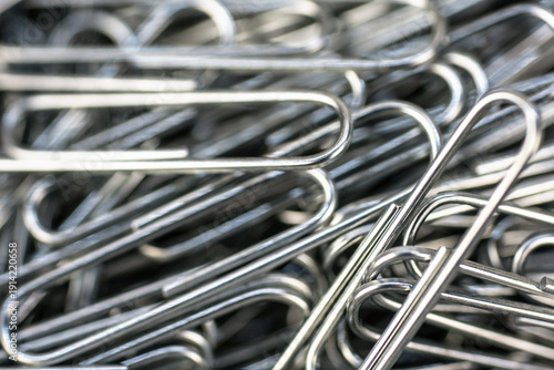 Close view of metal paper clips stacked on a surface with some clips overlapping each other during daylight hours