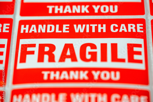 Labels that say fragile and handle with care are arranged on a surface for shipping items in a busy storage area during daytime hours