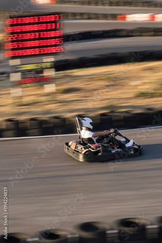 A person driving a go-kart speeds past the electronic scoreboard.