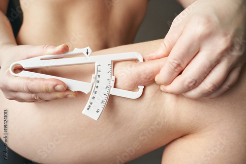 Schilderij op canvas Female adult measuring body fat with caliper on thigh for fitness and health assessment
