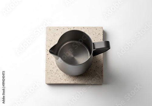 A minimalist overhead shot of a stainless steel milk pitcher resting on stone