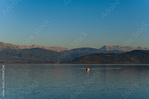 Bild auf Leinwand A single boat glides quietly across the calm surface of Lake Ioannina, with the distant Pindus mountains and gentle slopes forming a serene backdrop