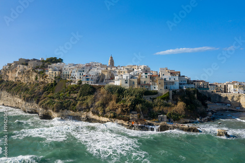 Canvastavla Historic whitewashed buildings cluster atop the rugged cliffs of Vieste, Italy, overlooking the churning turquoise waters of the Adriatic Sea