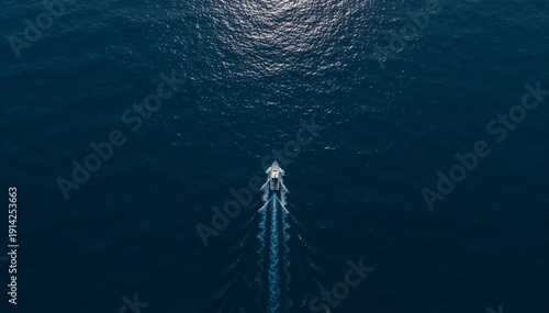 Aerial top view of a motorboat cruising in the deep blue ocean. Minimalist seascape with boat wake and sunlight reflection