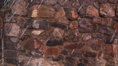 Old stone wall made of irregular rocks with mortar during rainfall. Natural masonry texture background. Construction and architecture material concept. Design for wallpaper, banner, poster.
