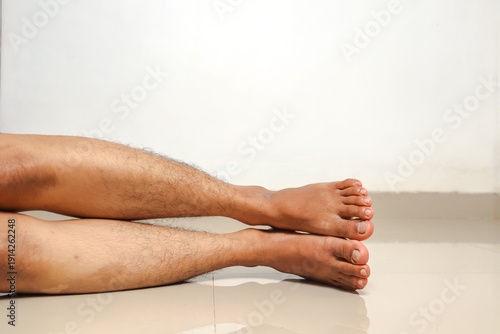 Man's legs and feet resting on a light tiled floor with white wall background
