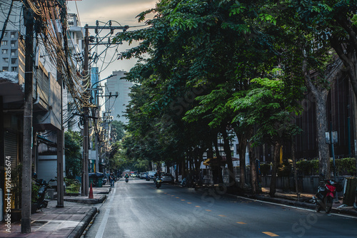 Typical Bangkok street at sunset with tropical trees and power lines, Cozy urban road in Thai city at dusk with greenery, motorcycles and cables overhead, Thailand