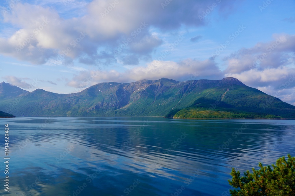 Fototapeta premium White clouds drift above a dramatic landscape of mountains and fjord in Helgeland, Norway.