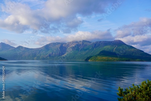 White clouds drift above a dramatic landscape of mountains and fjord in Helgeland, Norway.