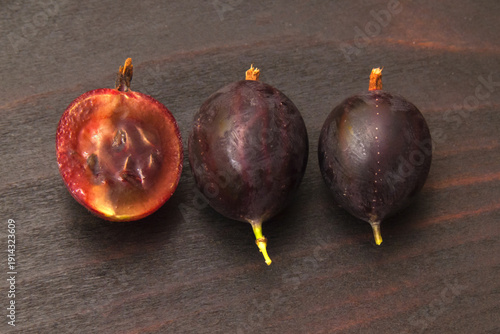 Three ripe gooseberry fruits in a row on dark wood