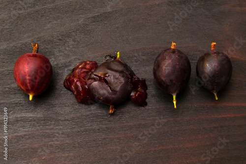 Whole and crushed gooseberry berries on dark wood