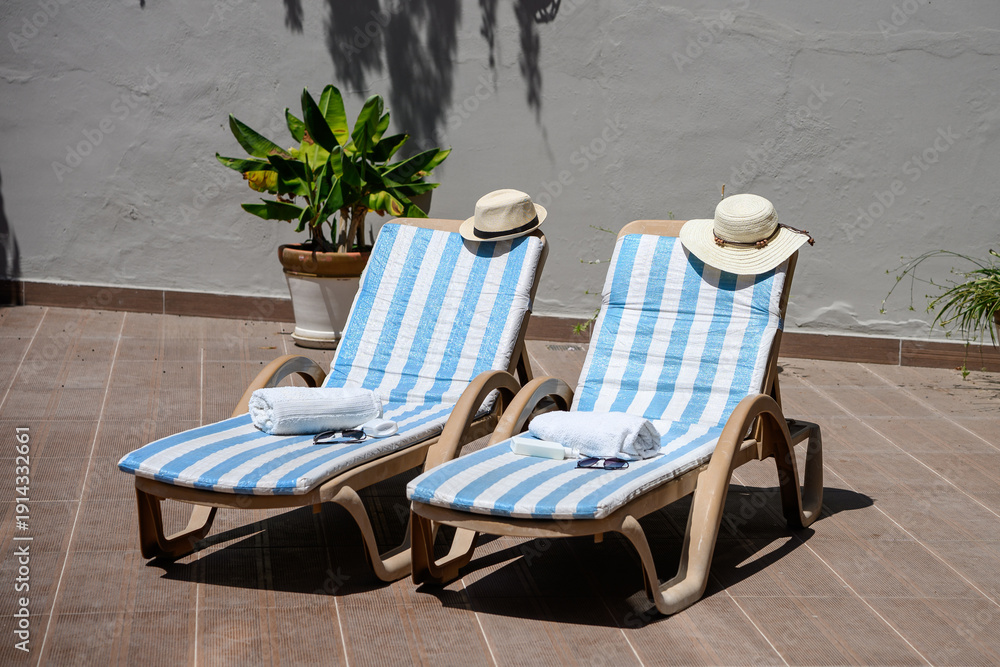 Fototapeta premium Cozy outdoor lounge area. Sun-drenched lounge chairs in cozy open space with hats, towels, and sunglasses. Concept is tanning and summer relaxation.