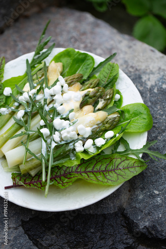 Fresh asparagus salad with arugula sorrel and creamy dressing on white plate copy space
