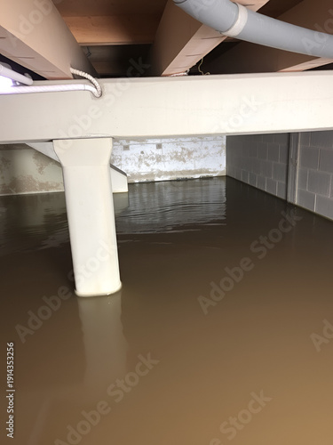 Flooded basement with standing water, beams, concrete walls, water damage consequences.
