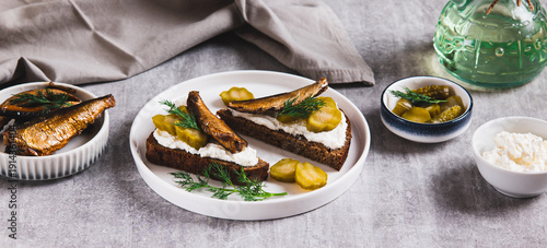 Obraz na plátne Sandwiches with ricotta, pickles and sprats on rye bread on a plate on a table w