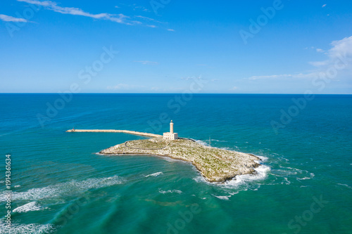 Obraz na płótnie Santa Eufemia lighthouse stands on a rocky island off the coast of Vieste, Italy, surrounded by turquoise Adriatic waters and an expansive blue sky