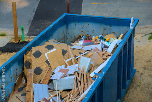 Fotografie Construction debris fills large blue waste dumpster near street