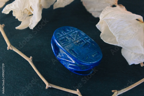 Lapis lazuli scarab base with engraved ancient egyptian hieroglyphs on dark stone with white petals.