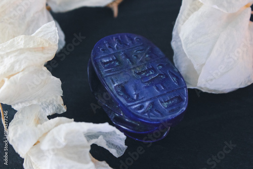 Lapis lazuli scarab base with engraved ancient egyptian hieroglyphs on dark stone with white petals.