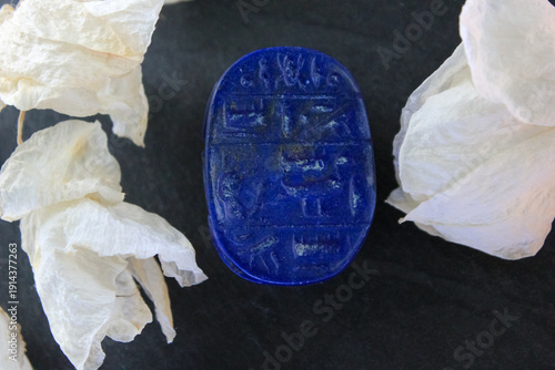 Lapis lazuli scarab base with engraved ancient egyptian hieroglyphs on dark stone with white petals.