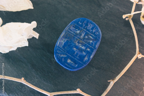 Lapis lazuli scarab base with engraved ancient egyptian hieroglyphs on dark stone with white petals.