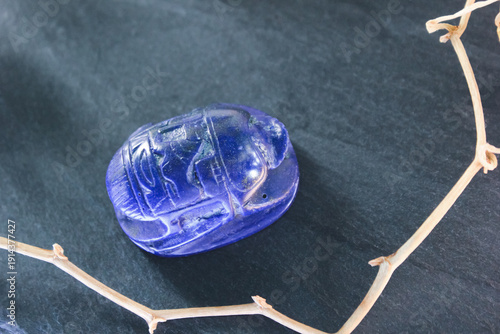 Lapis lazuli scarab beetle carving on dark slate stone with decorative dry branches, ancient amulet.