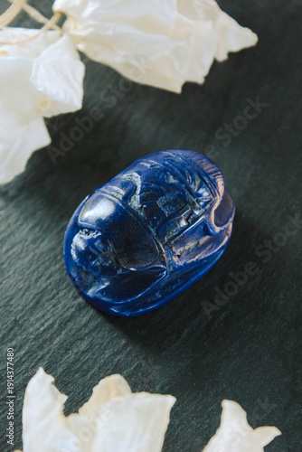 Beautiful lapis lazuli scarab beetle with dried white petals on a dark slate stone, ancient charm.