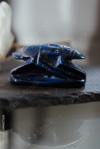 Side view of a blue lapis lazuli scarab beetle figurine on a dark stone surface, ancient talisman.