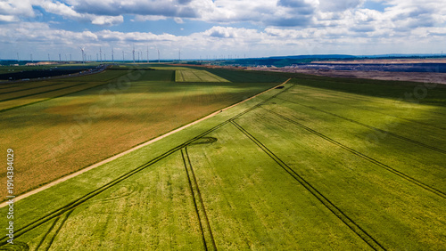 Scenic industrial landscape showing the contrast between traditional agriculture and modern energy production with wind farms and a thermal power station under a summer sky