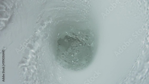 Close-up top view inside toilet bowl during flush. Water forms strong swirling vortex, moving toward drain hole. Hygiene concept, bathroom plumbing system in action, slow motion shot